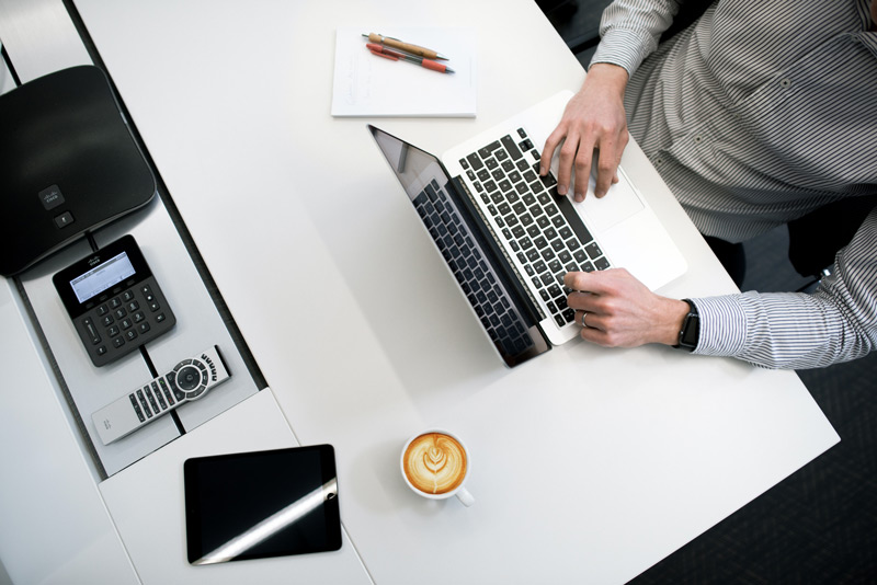 top-down picture of an office worker at a desk with laptop, coffee and other devices